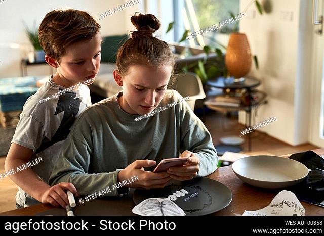 Brother and sister at home using smartphone for a creative online tutorial