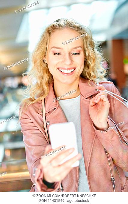 Junge Frau beim Shopping liest eine SMS auf dem Smartphone und freut sich