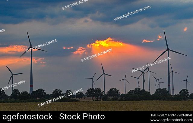 13 July 2022, Brandenburg, Mallnow: Colorful sunset shines through a gap in the clouds over the landscape with wind turbines. Photo: Patrick Pleul/dpa