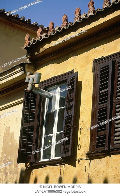 Shuttered windows with pipe sticking out and ornate edging to the roofline of house in Plaka
