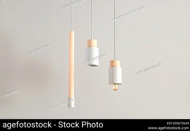 Several gray lamps with light wooden parts are hanging on the cables on the gray wall background. One lamp has an edison bulb. Closeup. Horizontal