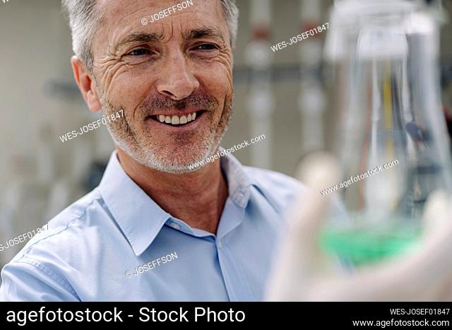 Close-up of smiling businessman holding conical flask in greenhouse