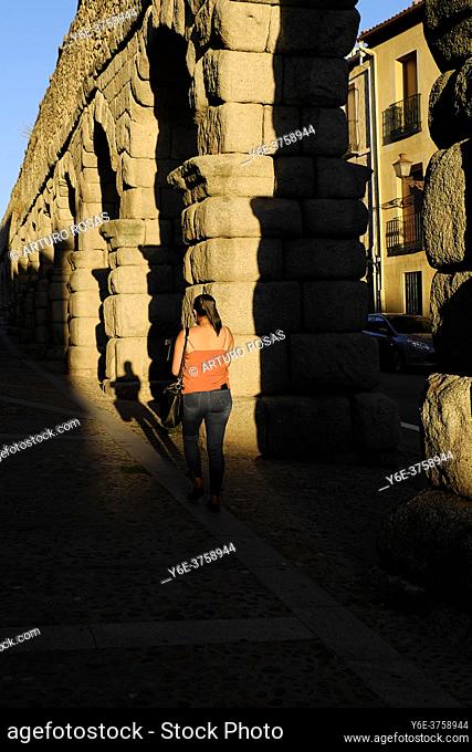 A woman walking next to the start of the acqueduct of Segovia