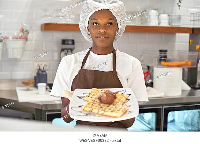 Young woman working in ice cream parlour, serving waffles with icecream