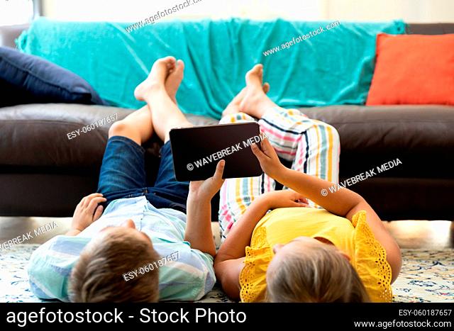 Caucasian brother and sister using tablet with blank screen lying on floor at home
