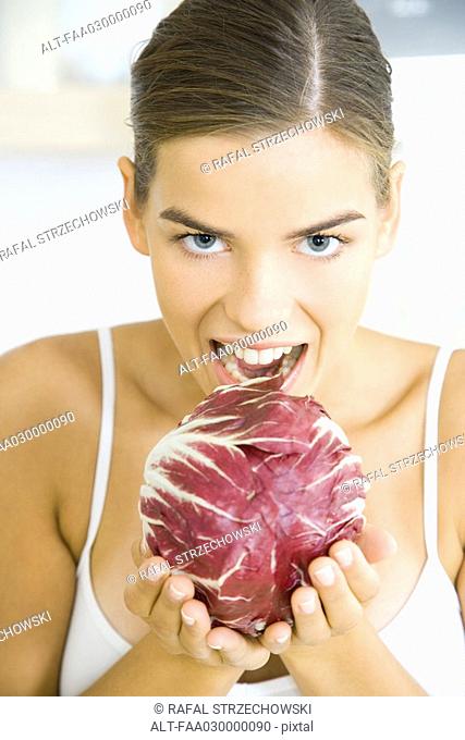 Woman holding up head of radicchio lettuce, ready to take a bite out of it
