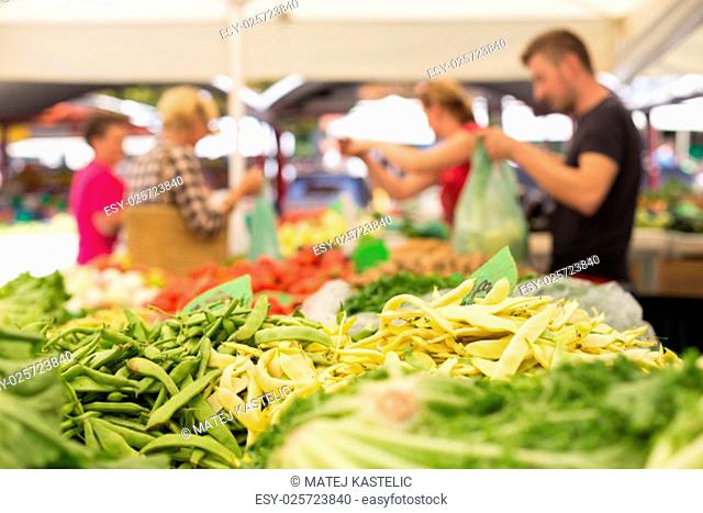 Farmers&#39; food market stall with variety of organic vegetable. Vendor serving and chating with customers