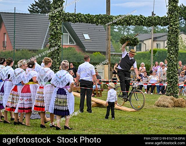 12 August 2023, Brandenburg, Heinersbrück: A participant in the traditional Sorbian-Wendish wreath piercing, tries to get a wreath off a holder with a stick...
