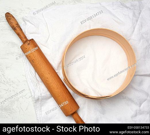 vintage wooden rolling pin and a round sieve lie on a white linen napkin, top view