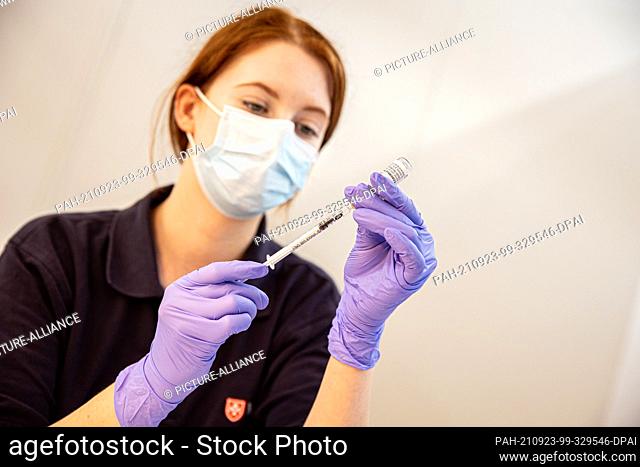 23 September 2021, Lower Saxony, Hanover: A helper draws up a syringe with Corona vaccine in a vaccination booth at the vaccination centre on the exhibition...