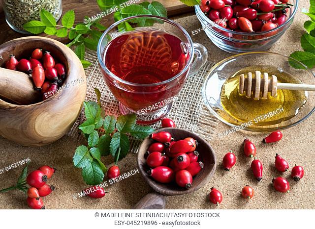 A cup of rose hip tea on a table, with fresh rosehips in the background