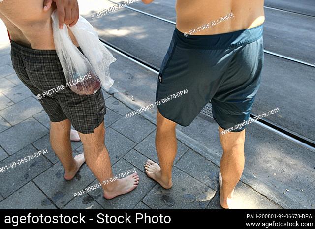 01 August 2020, Bavaria, Munich: Eisbach swimmers are standing at the Tivolistraße tram stop with a plastic bag in their hands