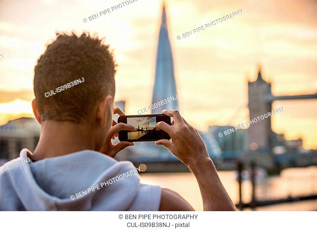 Man by riverside taking photograph of Tower Bridge and The Shard, Wapping, London, UK