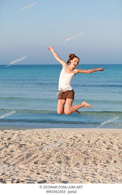 Junge fröhliche frau mädchen springt in die Luft am Strand im Sand morgens am meer im Sommer Urlaub