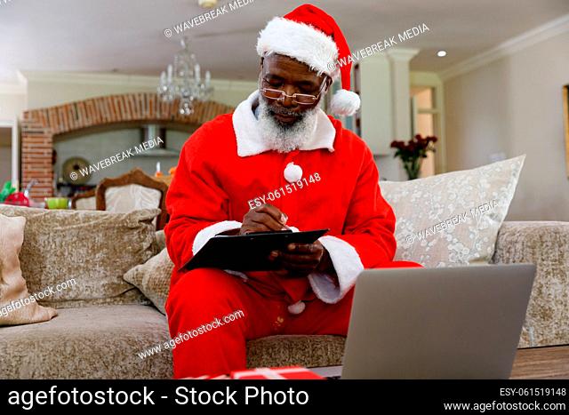 Senior african american man wearing a costume of santa claus and writing on clipboard