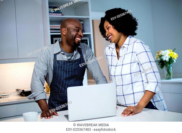 Cheerful couple using laptop in kitchen