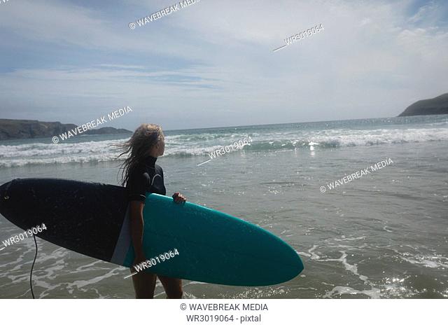 Female surfer standing with surfboard on beach