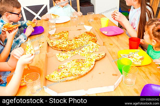 Children eating pizza, wooden table in the room, friends party