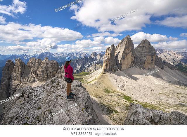 Young woman admiring the landscape around the Three Peaks of Lavaredo from the summit of Mount Paterno, in summer. Sesto Dolomites, Trentino Alto Adige, Italy