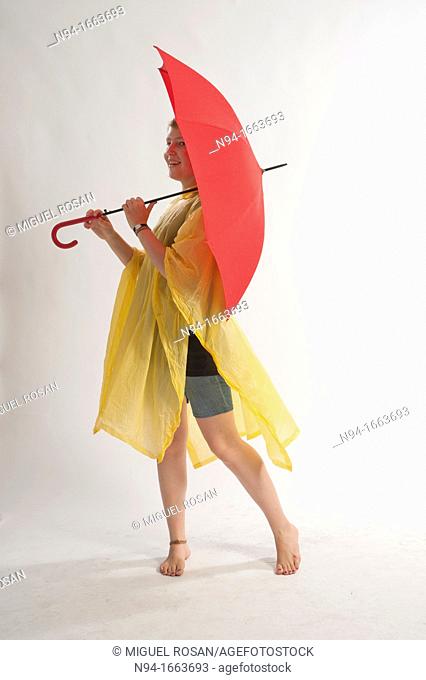 Teenage girl with yellow rain gear protected with red umbrella