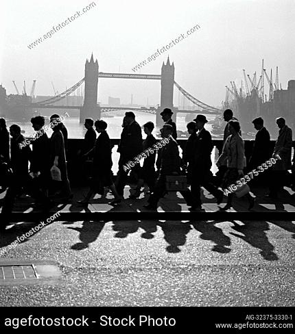 Pedestrians walking across London Bridge, with Tower Bridge visible in the background. Photographed by John Gay during the 1960s
