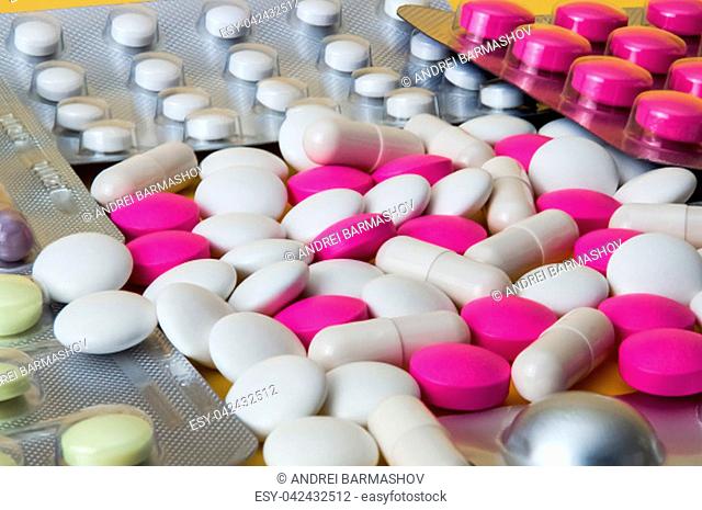 White and pink tablets are scattered among blisters with other pills. Large