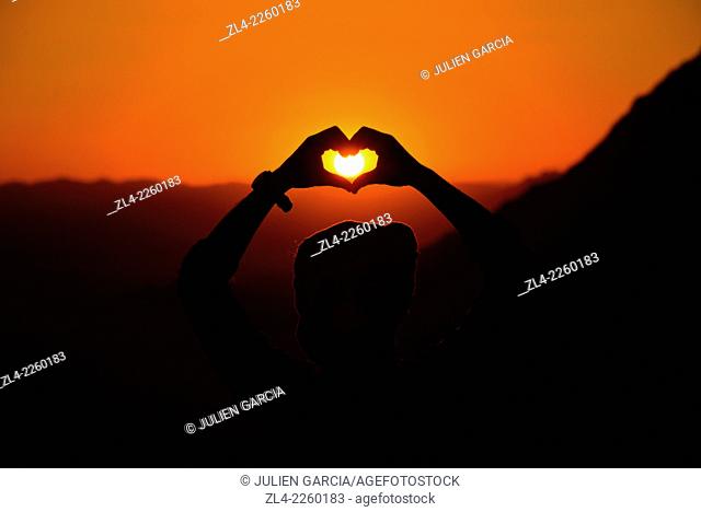Silhouette of a man making a heart shape with his hands at sunset. Jordan, Wadi Rum desert, border with Saudi Arabia