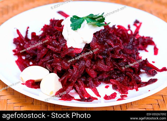 Grated beets with garlic in a plate on the table close-up