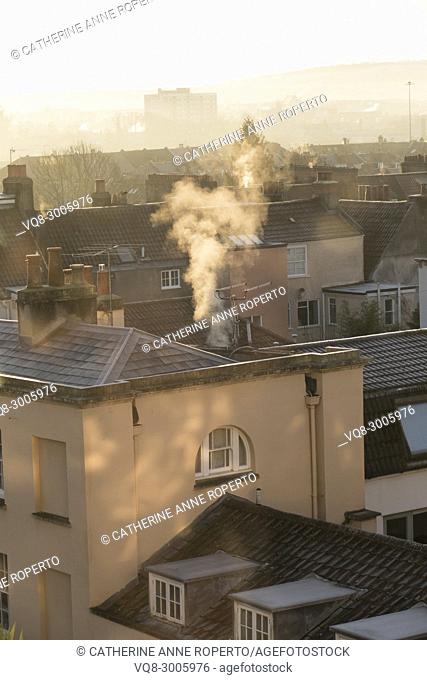 Dappled sunlight and plumes of white smoke curling upwards on a frosty day from the historic rooftops of Hotwells, Bristol, England