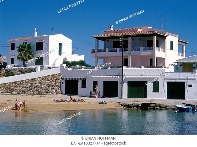 Balearic Island. White washed villas/ houses on sandy beach. Sand castle. People sunbathing. Sea
