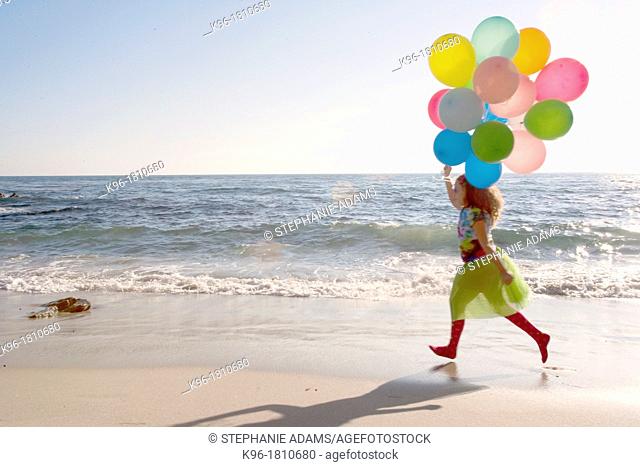 Young girl running along a beach with colorful balloons
