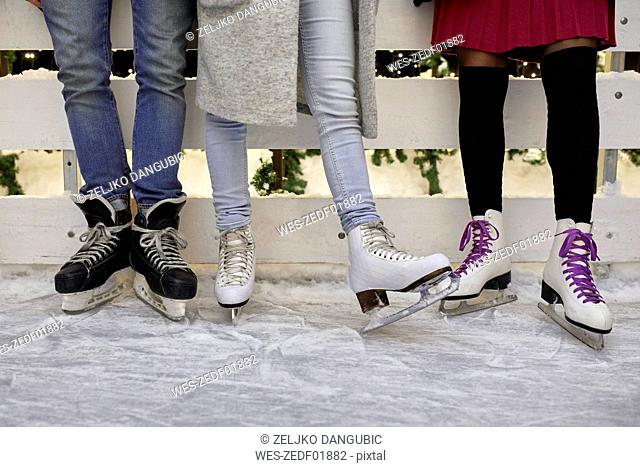 Legs of friends wearing ice skates standing at an ice rink