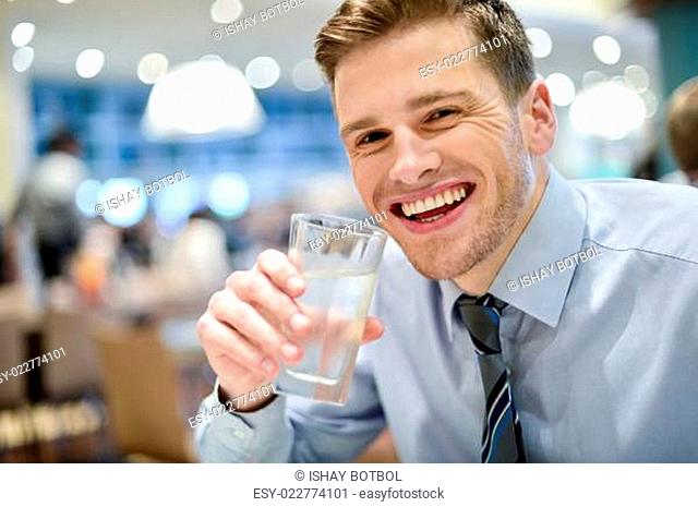 Smiling young man drinking water in restaurant