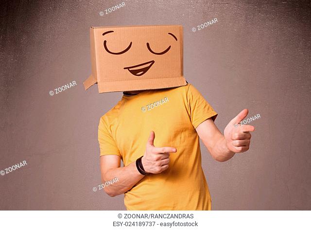 Young man gesturing with a cardboard box on his head with smiley face