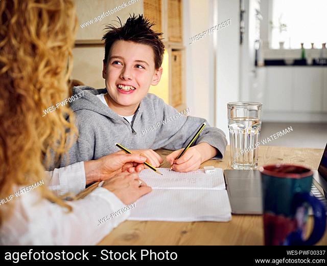 Son smiling while studying by mother at home