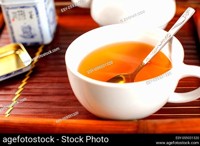 White porcelain cup of hot steaming tea, with spoon, placed on bamboo tray
