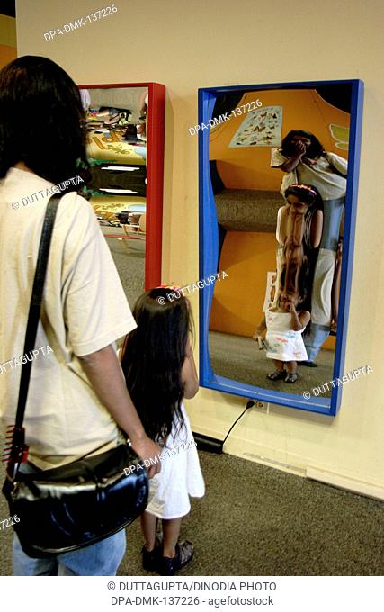 Girl with mother looking at concave and convex mirror in museum