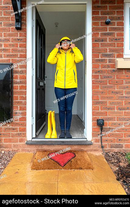 Woman wearing raincoat standing on doorway at home during rainy season