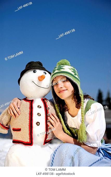 Girl wearing a dirndl beside a snowman, Frauenalpe, Murau, Styria, Austria