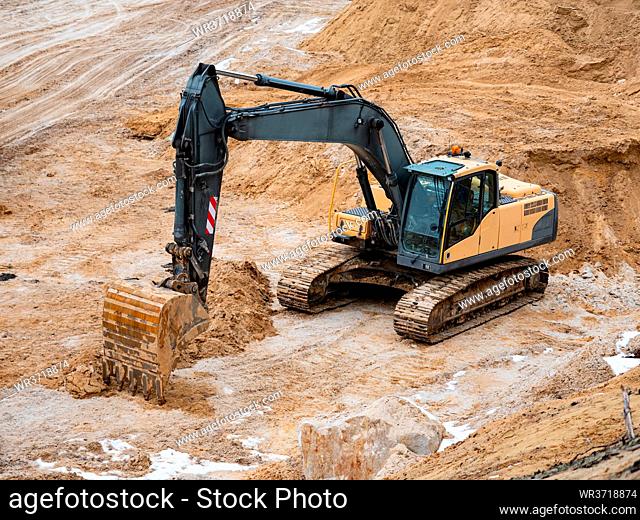 Track type loader excavator in large white sand quarry. Excavator loader machine during earthmoving works outdoors at construction site