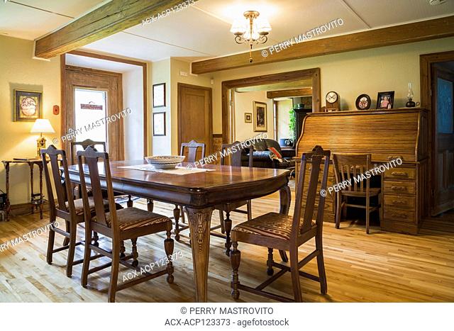 Dining room with antique wooden table and upholstered high-back chairs, roll top desk inside an old circa 1752 Canadiana style fieldstone house, Quebec, Canada
