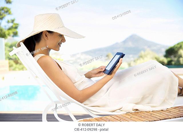 Woman using digital tablet on lounge chair at poolside