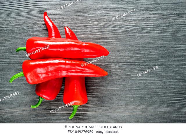 Five ripe sweet red Kapia peppers lying as sharp symbol on dark shale stone background