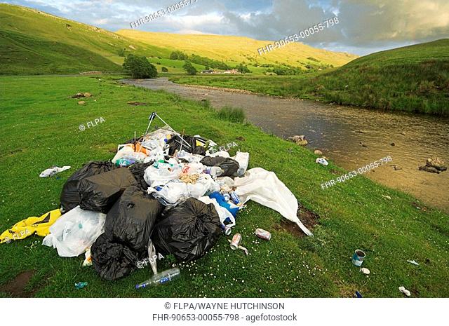 Fly-tipping in countryside, plastic bags full of rubbish, River Eden, Cumbria, England