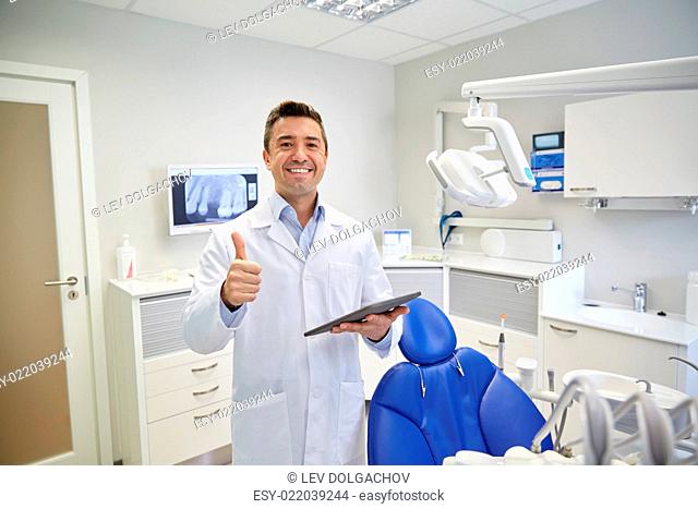 people, medicine, stomatology and healthcare concept - happy middle aged male dentist in white coat with tablet pc computer showing thumbs up at dental clinic...