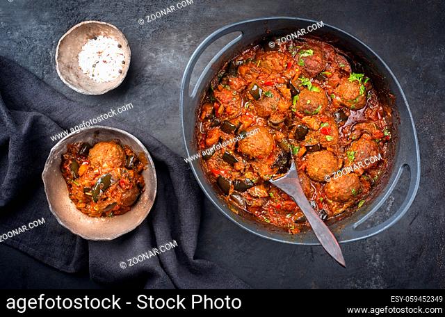 Traditional slow cooked American Tex Mex meatballs with eggplant with mincemeat in a spicy sauce offered as top view in a design cast-iron roasting dish