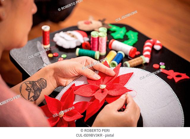 Woman stitching felt poinsettia onto christmas decoration, over shoulder view