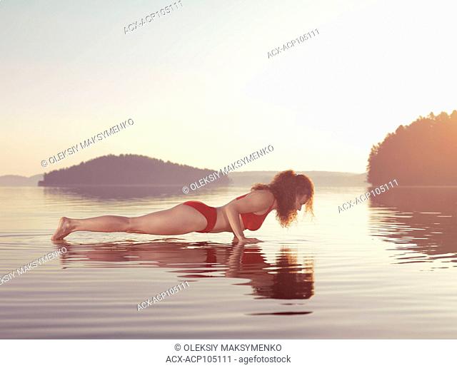 Young woman practicing Hatha yoga on a floating platform in water on the lake during misty sunrise in the morning. Yoga or pilates Plank posture, Kumbhakasana