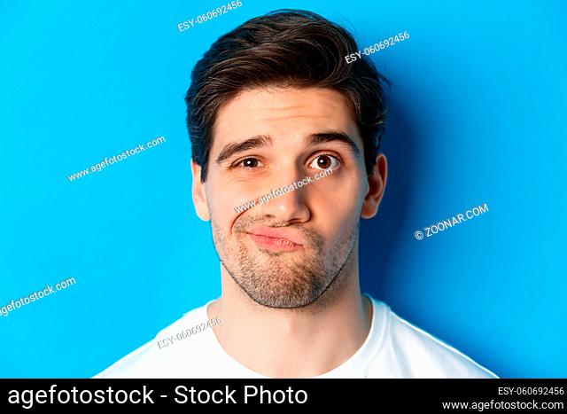 Headshot of skeptical guy looking at something unamusing, grimacing and standing reluctant against blue background