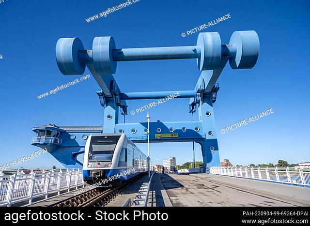 04 September 2023, Mecklenburg-Western Pomerania, Wolgast: A train passes men working with construction machinery on the B111 road bridge between Wolgast and...